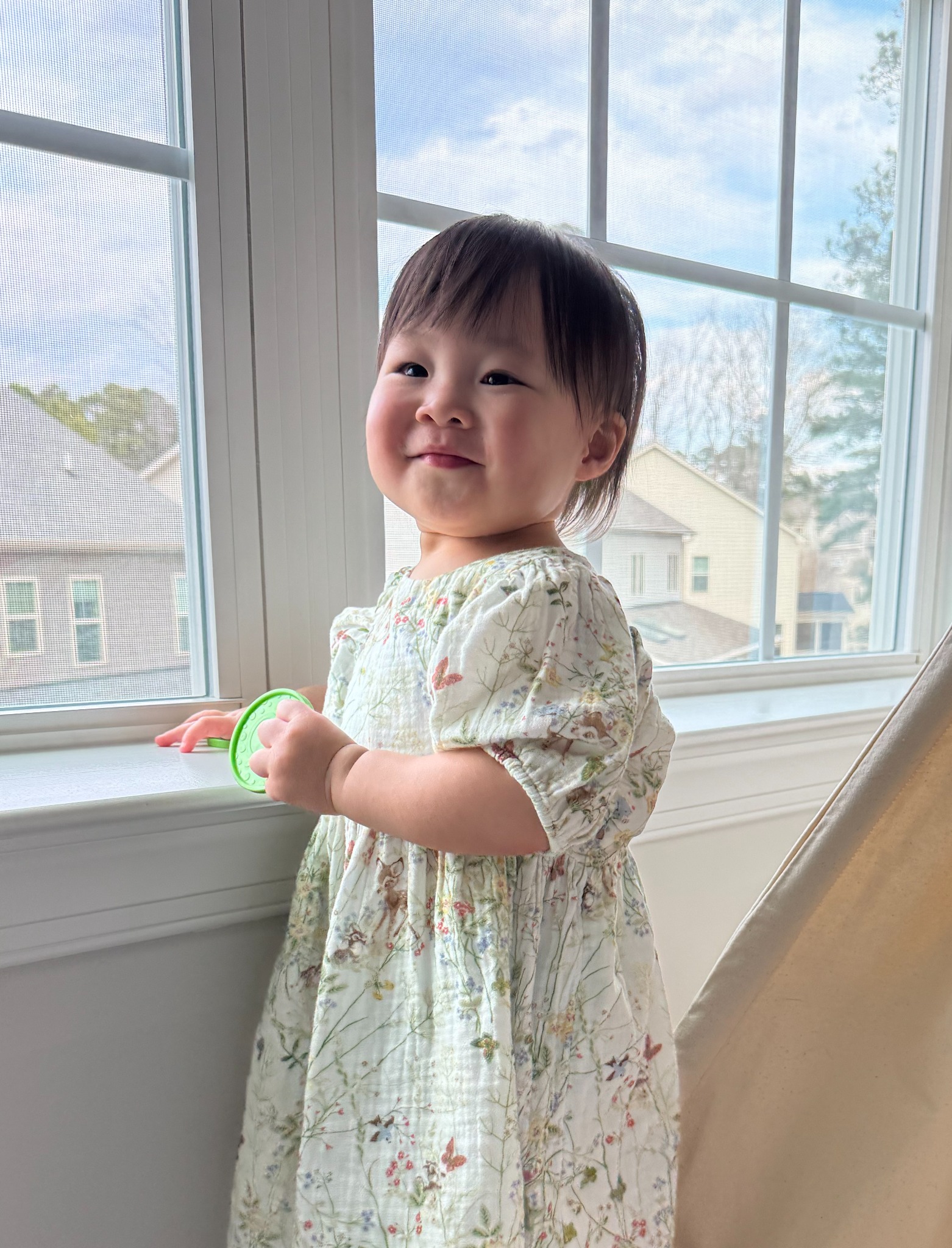 Diana smiling by a bright window in a floral dress.